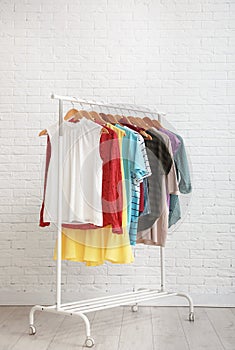 Wardrobe rack with stylish clothes near brick wall. Space for text
