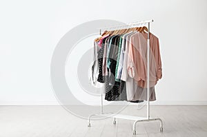 Wardrobe rack with stylish clothes near white wall. Space for text photo