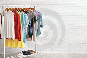 Wardrobe rack with stylish clothes and shoes near brick wall indoors.