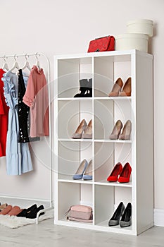 Wardrobe shelves with different stylish shoes and clothes indoors.