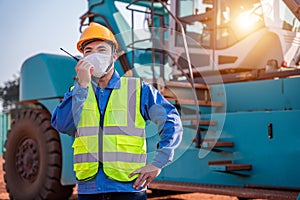 Warehouse asian man worker driver truck driver crane lifting up container with safety equipment, helmet is standing in front of