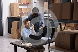 Warehouse employees analyzing transportation logistics on laptop computer while discussing metallic box order