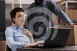 Warehouse employees looking at transportation logistics on laptop computer discussing cargo stock