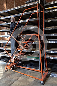 Warehouse factory working on a ladder pulling product from the racking