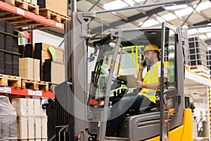Warehouse forklift driver holding smartphone, phone calling. Warehouse worker preparing products for shipmennt, delivery