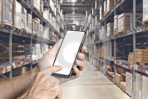 Warehouse with a hand holding an empty smartphone. Blurred industrial warehouse with goods and products. Logistics