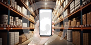 Warehouse with a hand holding an empty smartphone. Blurred industrial warehouse with goods and products. Logistics