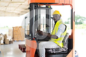 Warehouse man worker driver forklift. warehouse worker driver stacking card boxes by forklift in warehouse store. African American