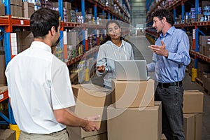 Warehouse manager carrying a box and his colleagues discussing