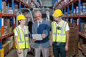 Warehouse manager and co-workers discussing over clipboard