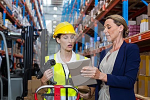 Warehouse manager with interacting female worker over digital tablet
