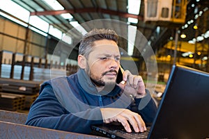 warehouse manager using telephone and laptop in large warehouse