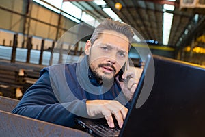 warehouse manager using telephone and laptop in large warehouse