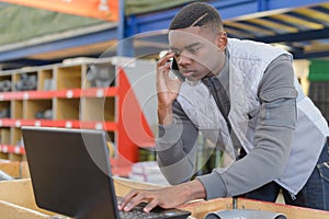 Warehouse manager using telephone and laptop in large warehouse