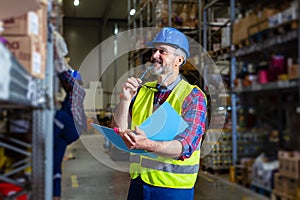 Warehouse manager writing on clipboard in a large warehouse