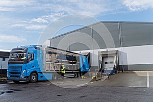 Warehouse receiver standing by blue truck, holding tablet, looking at cargo details, checking delivered items, goods