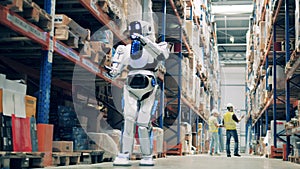 Warehouse robot scanning barcodes on cardboard boxes with two workers in the background