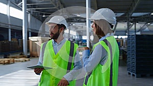 Warehouse specialists checking factory production holding tablet papers talking