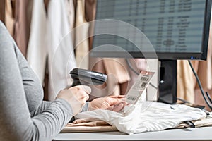 A warehouse woman employee accepts clothes using barcode scanner reading a bar code from price tag of female blouse