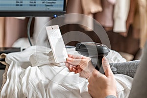 A warehouse woman employee accepts clothes using barcode scanner reading a bar code from price tag of female blouse