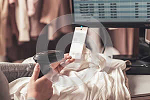 A warehouse woman employee accepts clothes using barcode scanner reading a bar code from price tag of female blouse