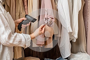 A warehouse woman employee accepts clothes using barcode scanner reading a bar code from price tag of female blouse