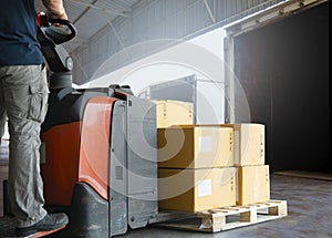 Warehouse worker driving electric forklift pallet jack loading shipment boxes into a truck.