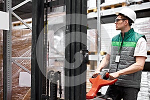 Warehouse worker with fork pallet truck stacker at modern warehouse