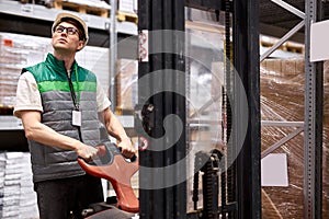 Warehouse worker with fork pallet truck stacker at modern warehouse