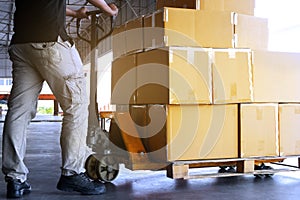 Warehouse worker with hand pallet truck unloading shipment boxes on pallet.