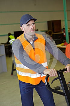 Warehouse worker in high-vis vest pushing pallet truck