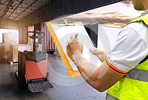 Warehouse worker holding clipboard checking on checklist for loading shipment goods into container truck.