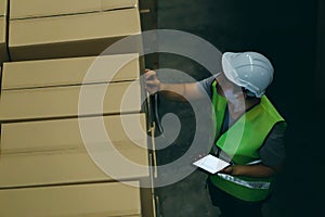 Warehouse worker man with safety hard hat is checking order details with a digital tablet at inventory room