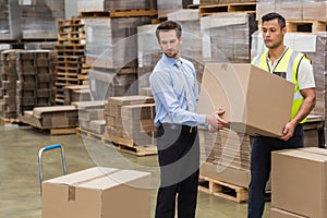 Warehouse worker and manager carrying a box together