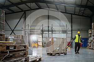 Warehouse worker maneuvering pallet jack loaded with goods through warehouse.