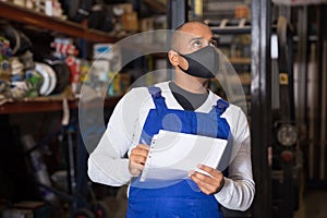 Warehouse worker in protective mask making notes during inventory of building materials