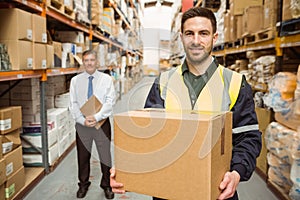 Warehouse worker smiling at camera carrying a box