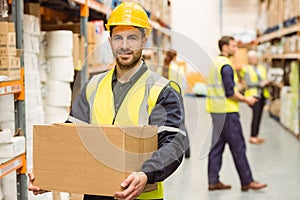 Warehouse worker smiling at camera carrying a box