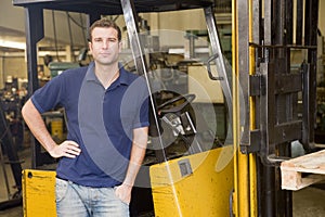 Warehouse worker standing by forklift