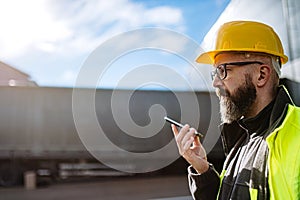 Warehouse worker standing outdoors, phone calling with truck driver. Warehouse receiver waiting for a delivery.