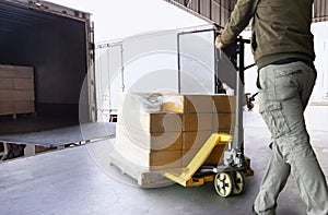 Warehouse worker unloading cargo shipment goods, his using hand pallet jack load into a truck.