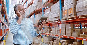 Warehouse worker using digital tablet while talking on mobile phone