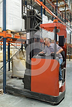 warehouse worker using fork truck to load pallet on racking