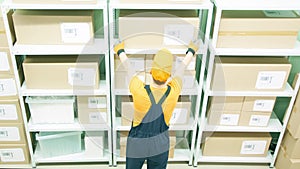 Warehouse worker wearing orange and blue uniform puts a big box on the storage shelf