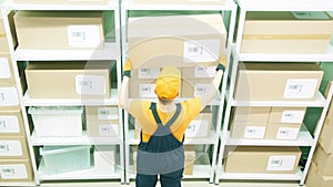 Warehouse worker wearing orange and blue uniform puts a big box on the storage shelf