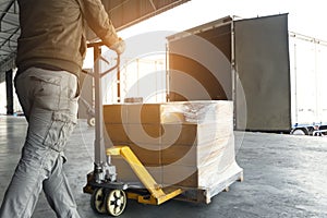 Warehouse worker working with hand pallet truck loading package boxes on pallet into cargo container.