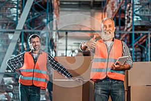 cheerful warehouse workers with digital tablet smiling at camera and showing photo