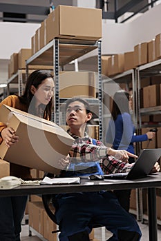 Warehouse workers holding parcel and scheduling delivery on laptop