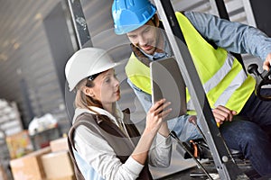 Warehouseman driving cart with coworker photo