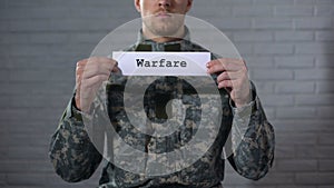 Warfare word written on sign in hands of male soldier, military conflict